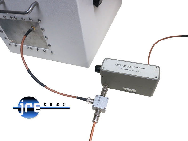 Bench setup: coaxial cable from a test enclosure I/O plate runs to a small power combiner, which feeds a Hewlett-Packard 355D step attenuator