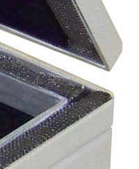 Close-up of the open corner of a test enclosure showing the knitted-mesh RF gasket running around the mating surfaces of the lid and body
