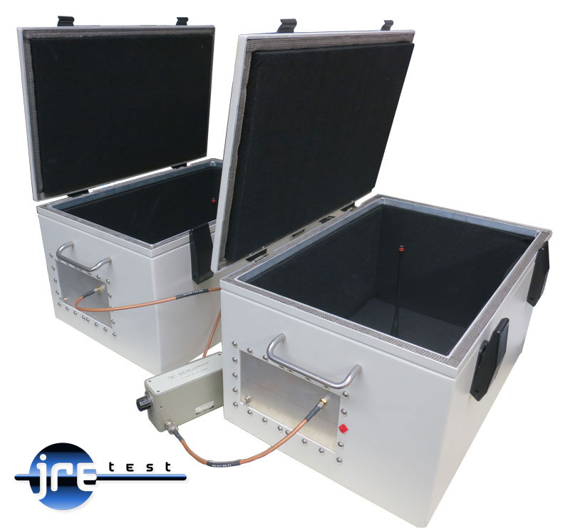 Two JRE 1812 test enclosures with lids open showing RF absorbing foam liners and internal antennas, connected through a step attenuator sitting on the bench between them