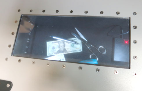 A shielded viewing window set into the wall of a JRE 1812WS enclosure, with the lit interior and the items inside clearly readable through the glazing